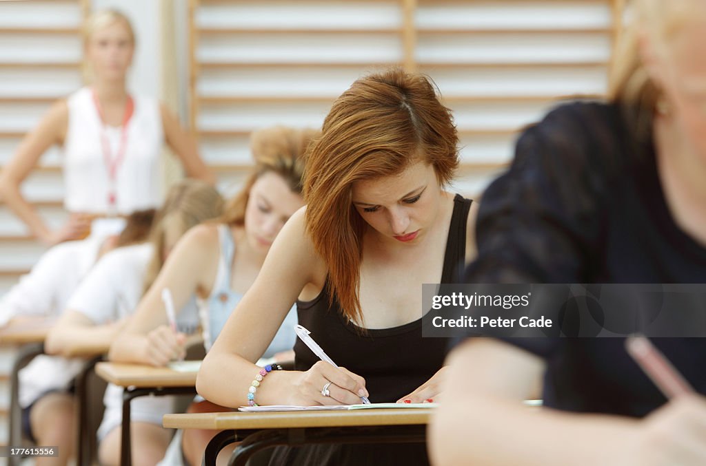 Students taking exam, teacher in background