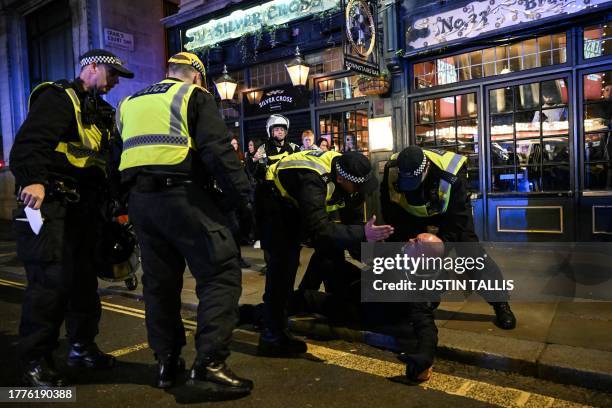 Police officers detain a man in the street by Whitehall close to the 'National March For Palestine' in central London on November 11 as...