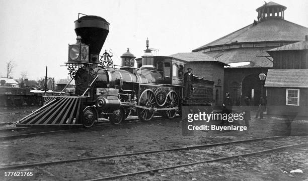 View of the ornately decorated locomotive J.H. Devereux, of the United States Military Railroad, with two crew members on board outside the...