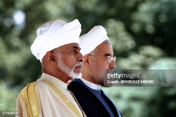 Iranian President Hassan Rowhani and Oman's Sultan Qaboos bin Said listen to the national anthems during a welcome ceremony at Tehran's Saadabad...