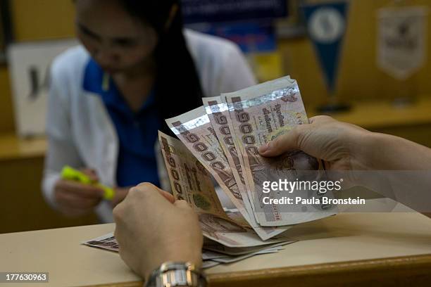Woman counts Thai bhat before depositing at a local bank on August 23, 2013 in Bangkok, Thailand. The local currency dropped to its lowest level...