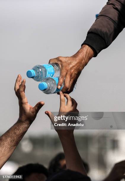 Palestinian man, suffering from clean water shortage, takes water bottle from personnel as those, who have migrated from the northern to the southern...