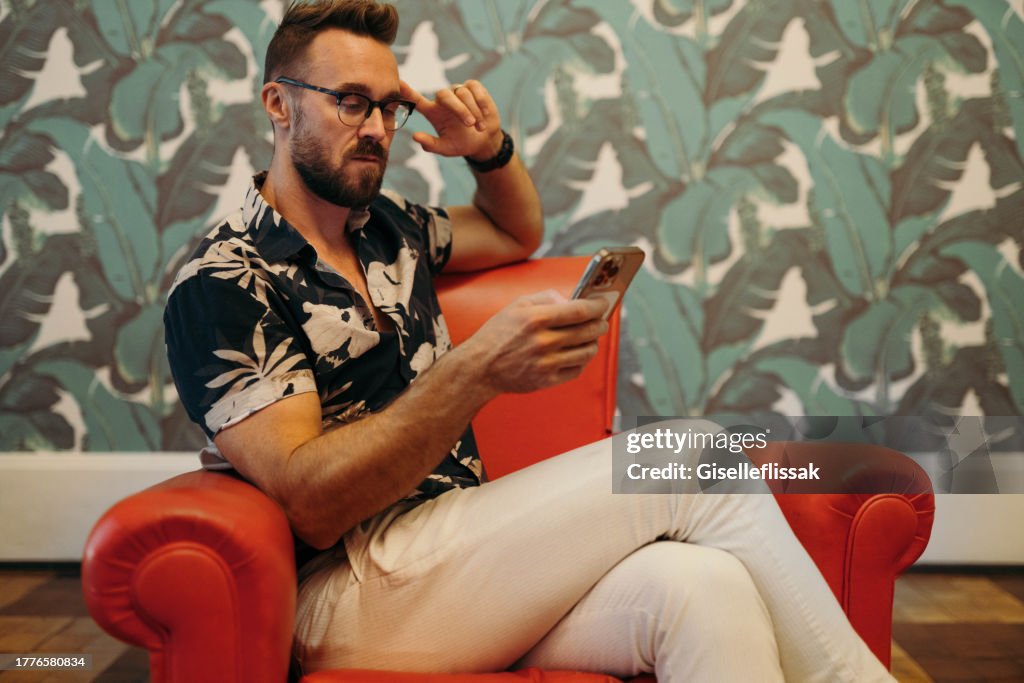 自宅の椅子に座りながら携帯電話のメッセージをチェックするスタイリッシュな男性