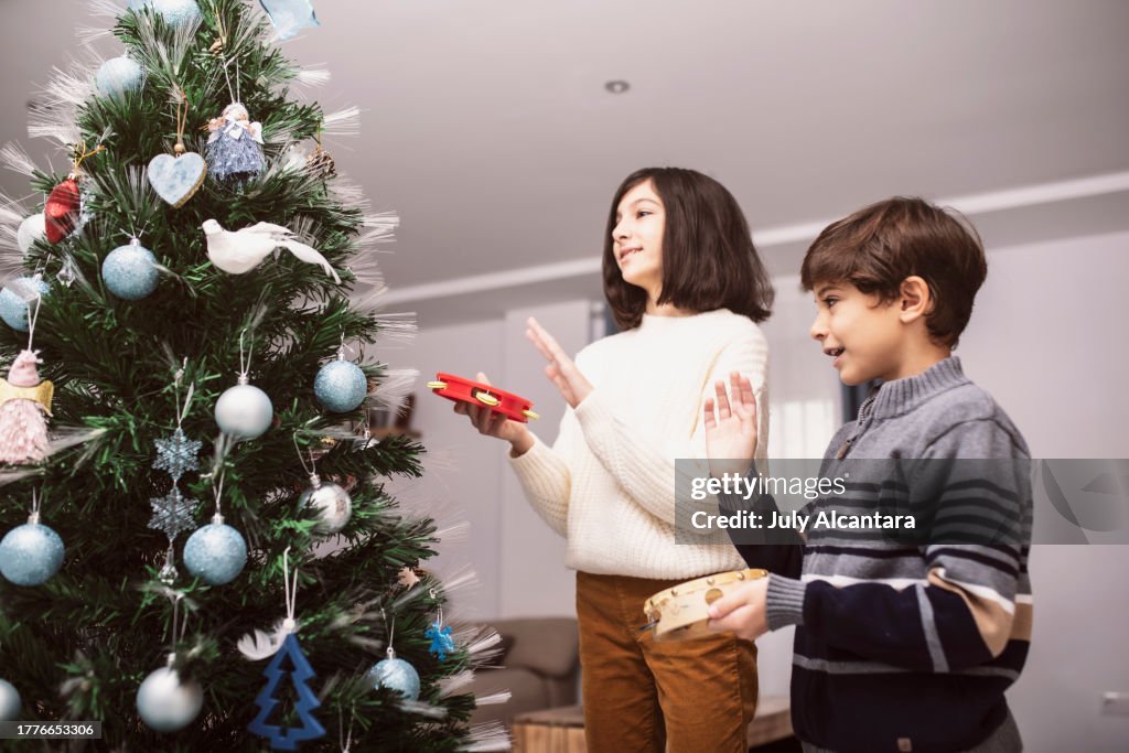 Kinder spielen das Tamburin neben ihrem Weihnachtsbaum
