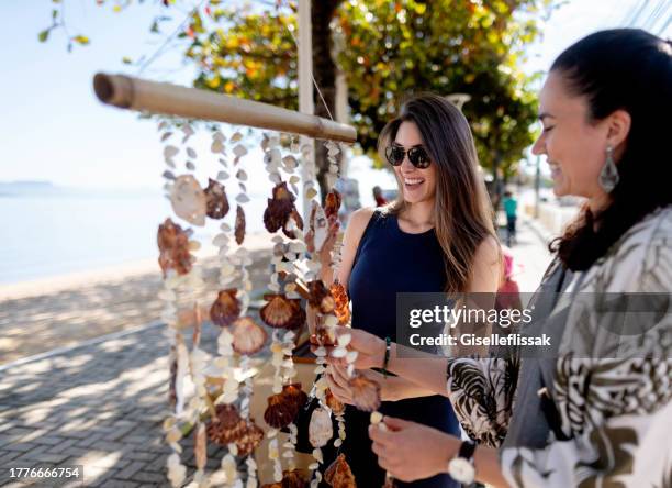 two friends looking at seashell curtain hanging outdoors - handwerkprodukten stockfoto's en -beelden