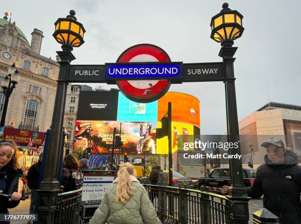 People pass the illuminated London Underground sign above the entrance to a station on October 23, 2023 in London, England. With an array of notable...