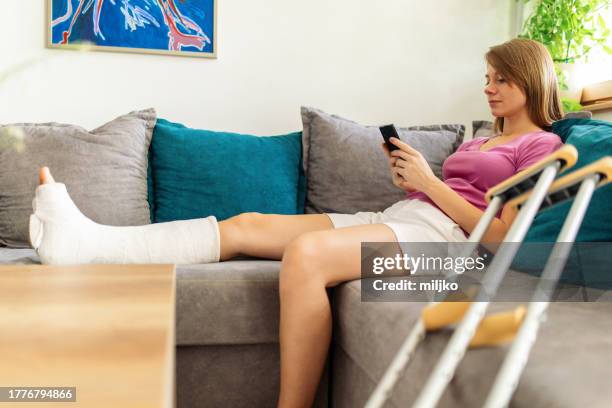 frau mit gips am bein schreibt sms am telefon - orthopedic cast stock-fotos und bilder