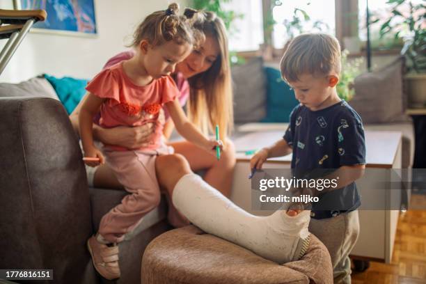 mutter mit ihren beiden kindern schreibt auf gips an ihrem bein - gipsverband stock-fotos und bilder