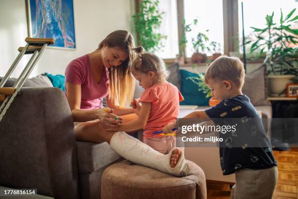 mother with her two children writing on cast on her leg - gips bouwmateriaal stockfoto's en -beelden