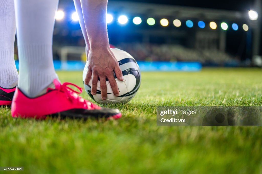 Soccer player putting sports ball on grass