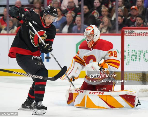 Dustin Wolf the Calgary Flames tries to control the puck with Mathieu Joseph of the Ottawa Senators looking for a rebound during the third period at...