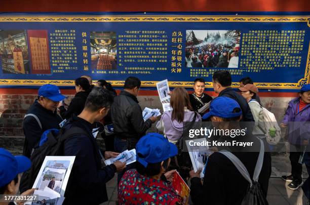 Chinese tourists look at photos they purchased from a tour guide, centre right, of their visit to the capital citys tourist sites while standing...