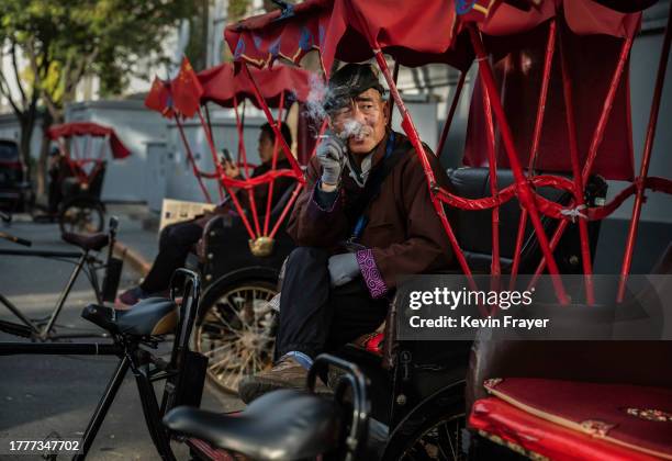 Rickshaw driver smokes as he and others wait for tourists near the Shichahai Lake and Houhai Lake areas on November 3, 2023 in Beijing, China. Chinas...