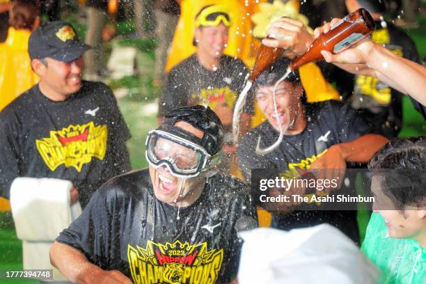 Head coach Akinobu Okada of Hanshin Tigers is poured beers as the team celebrates winning the Japan champions following the team's 7-1 victory in the...