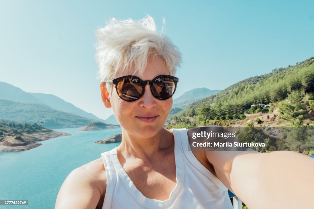 Smiling middle age woman taking selfie while walking alone in mountains in summer vacations