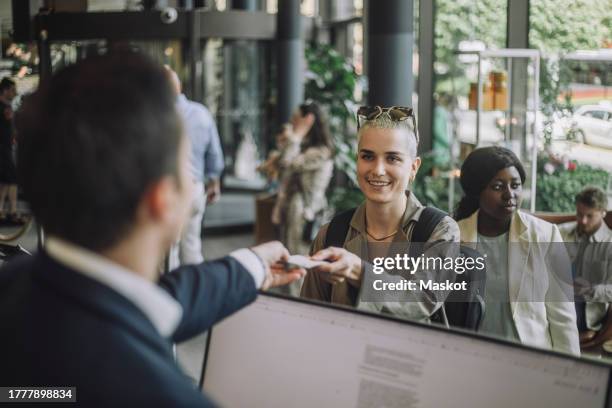 smiling non-binary person taking keycard from receptionist at hotel - hotel reception stockfoto's en -beelden