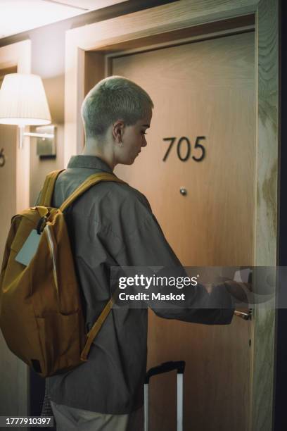 non-binary business person with backpack entering hotel room using keycard - keycard access stock pictures, royalty-free photos & images