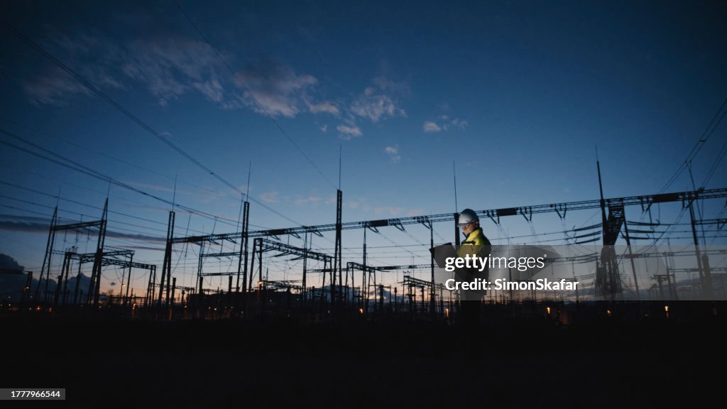 Ingegnere elettrico maschio che utilizza il laptop sulla centrale elettrica di Silhouette al crepuscolo