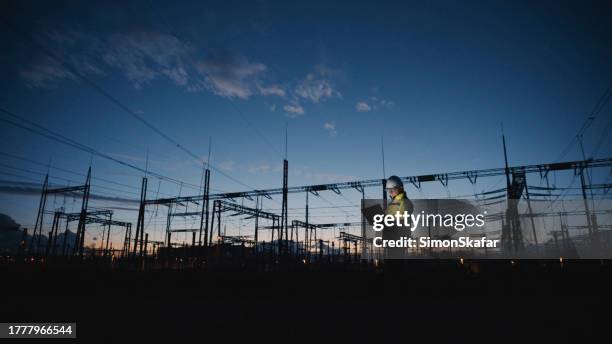 male electrical engineer using laptop on silhouette power plant at twilight - rede elétrica imagens e fotografias de stock