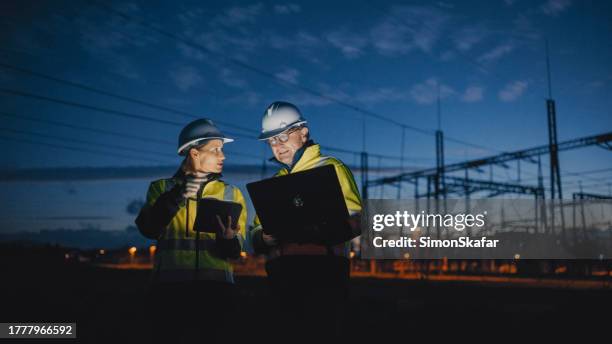 electrical engineers discussing over laptop and digital tablet while standing at dark power station during night - fuel and power generation stock pictures, royalty-free photos & images