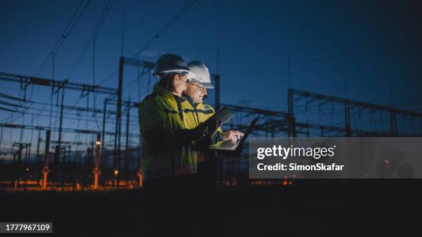 männliche und weibliche elektroingenieure diskutieren nachts über laptop im dunklen kraftwerk - kraftwerk stock-fotos und bilder