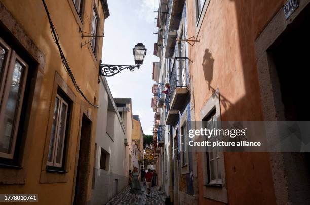 October 2023, Portugal, Lissabon: The shadow of a street lamp in a narrow alleyway in the Alfama district, where day-trippers walk along, can be seen...