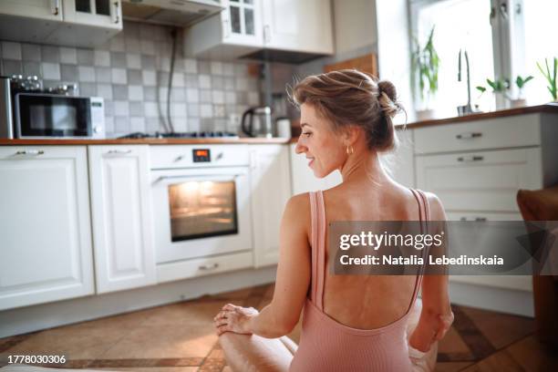 elegant middle-aged lady in sports swimsuit performing stretching exercises at home on a yoga mat. copy space and back view - cicatriz fotografías e imágenes de stock