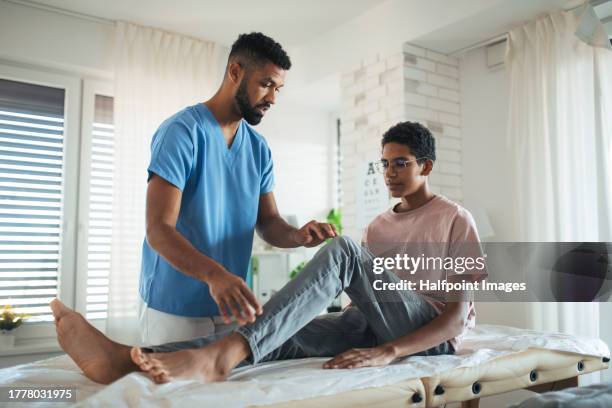 physiotherapist doing manual therapy, exercise with teenage boy's knee, rehabilitation. orthopedist examining and treating painful injured knee of young athlete. concept of preventive health care for adolescents. - gesundheitsvorsorge stock-fotos und bilder