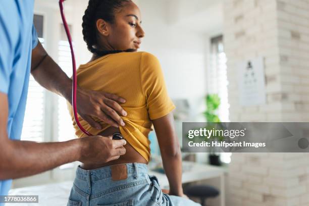 doctor listening to girl’s breathing, heartbeats using a stethoscope. teenage girl visiting paediatrician for annual preventive physical examination. concept of preventive health care for adolescents - prevención de enfermedades fotografías e imágenes de stock