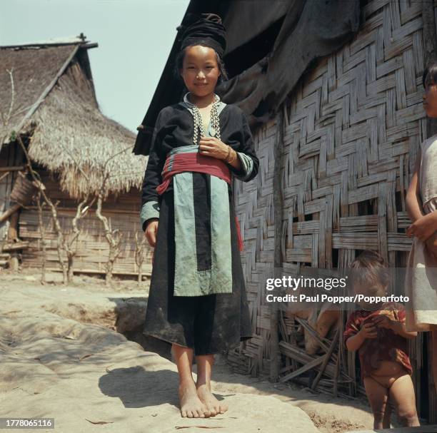 Portrait of a young woman of the Hmong people, a sub-group of the Miao people, standing next to a hut on a street in the city of Vientiane, capital...