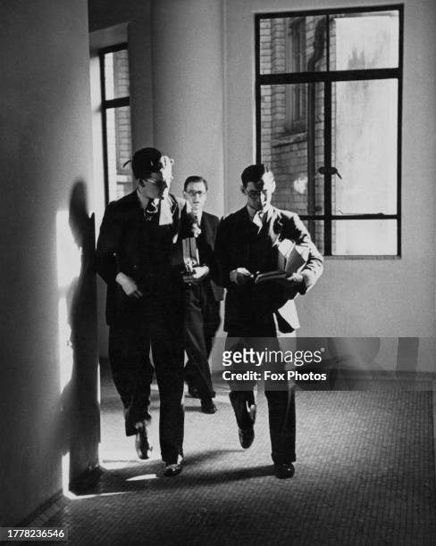 Group of three trainee doctors, one reading a book, as they walk down a corridor, an open window in the background, at a hospital, United Kingdom,...