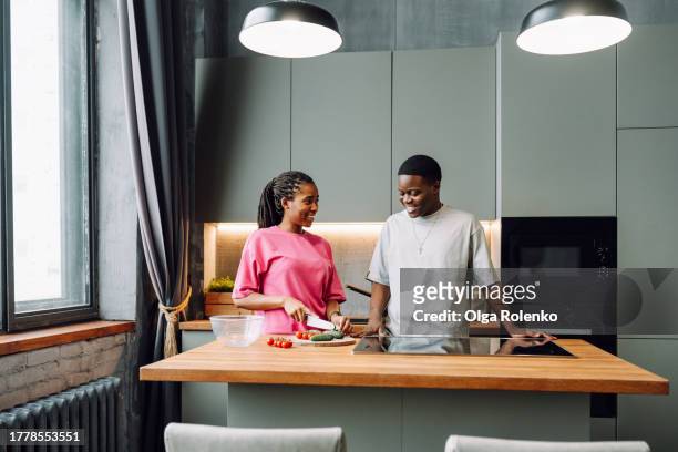 smiling dark skin couple cooking vegetable salad in the modern kitchen together - stove top stock-fotos und bilder