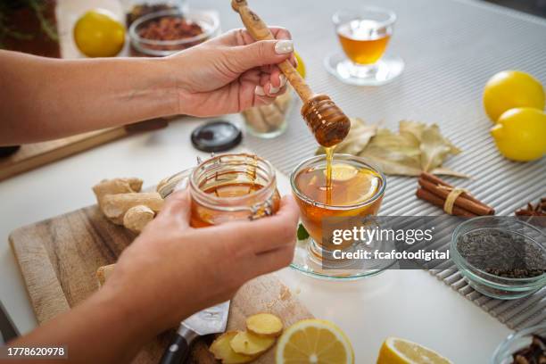donna che aggiunge miele a una tazza di tè allo zenzero e limone - bevanda calda foto e immagini stock