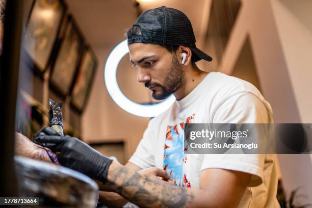 young tattoo artist tattooing his customer in his studio - graphic design studio stock pictures, royalty-free photos & images