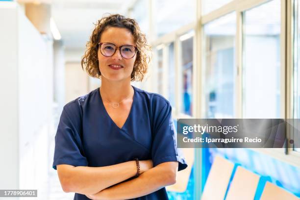 portrait of a curly-haired caucasian nurse with glasses in the hallway of the hospital or medical center with her arms crossed, medical team of the medical clinic - executivo chefe de operações - fotografias e filmes do acervo