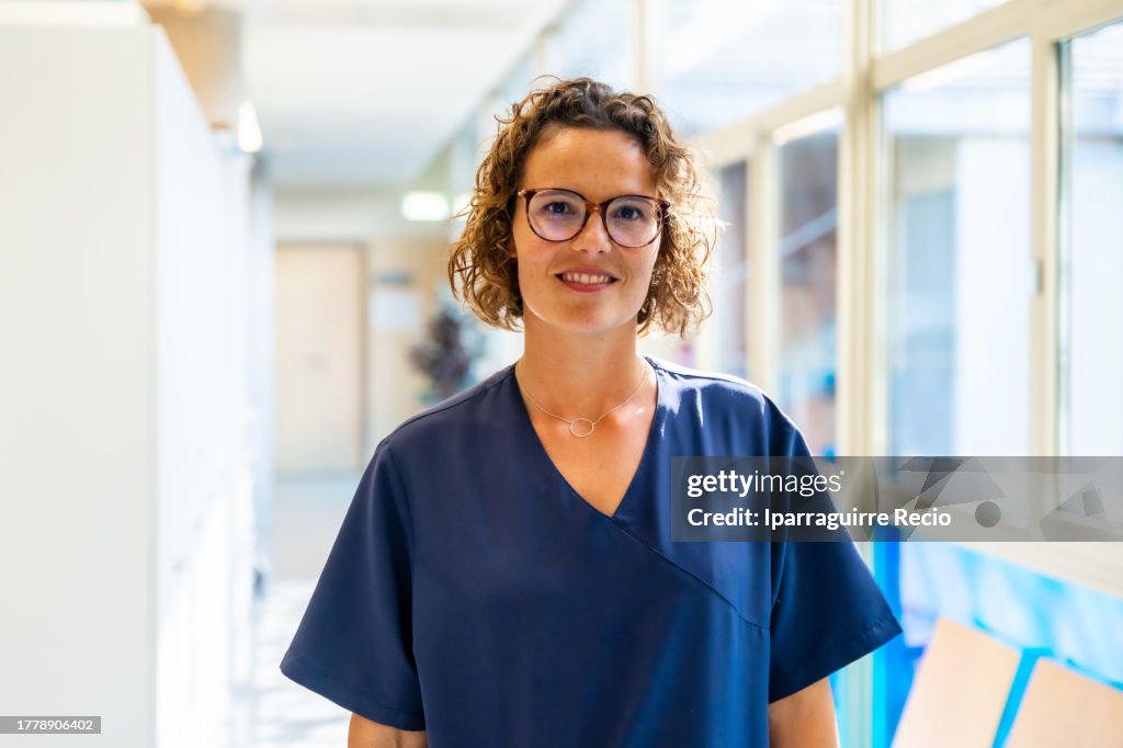 Portrait of a curly-haired Caucasian nurse with glasses in the hallway of the hospital or medical center, medical team of the medical clinic