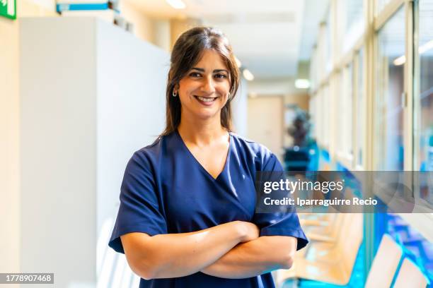 portrait of an attractive dark-haired nurse smiling in the hallway of the hospital or medical center with her arms crossed, medical team of the medical clinic - operations manager stock pictures, royalty-free photos & images