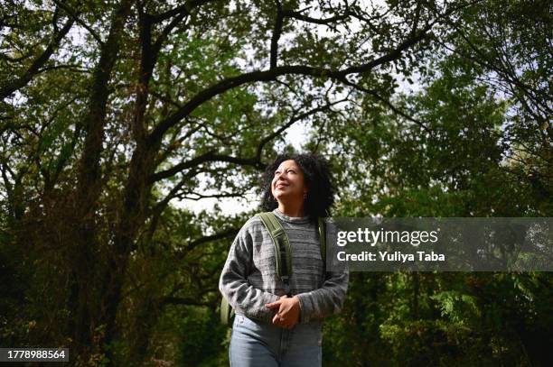 multiracial woman with curly hair standing in a woodland and admiring the nature. - verwonderingsdrang stockfoto's en -beelden