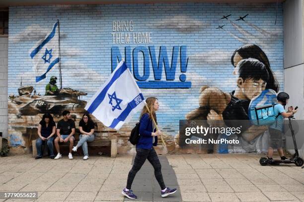 An Israeli woman carries an Israeli flag as she passes in front of a graffity calling for the release of Israelis held hostage by Hamas in Gaza in...