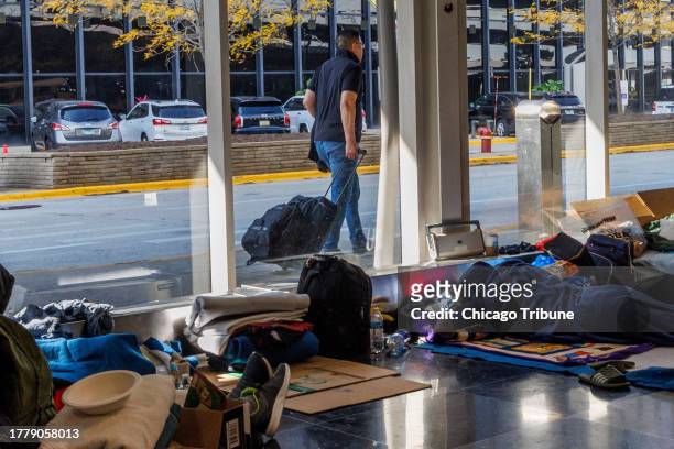 Traveler walks by a window while migrants lie on the ground at a makeshift shelter at O'Hare International Airport on Oct. 24 in Chicago.