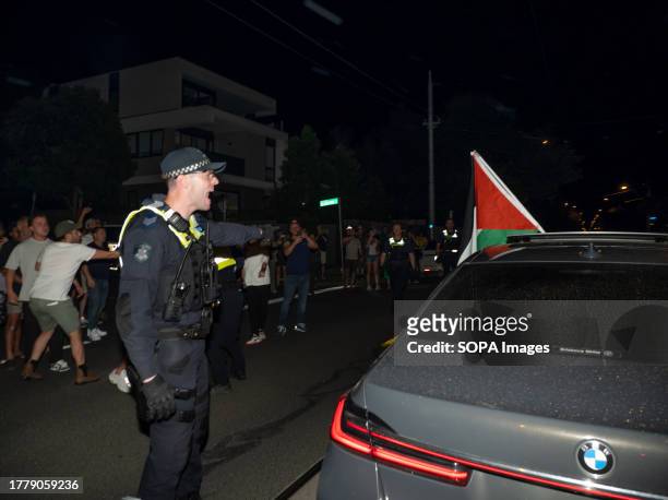 Police officer shouts at a driver to move his car displaying a Palestian flag as he stops in the road. Pro-Israel counter-protesters hold back a...