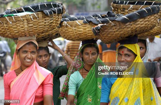 Indian women dressed in their different coloured traditional saris carry plastic-lined cane baskets on their heads as they return from market in the...
