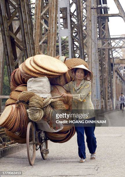 Woman walks with a bicycle loaded with bamboo baskets on the old Long Bien bridge crossing the Red River as she heads to a market in the centre of...