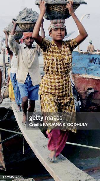 Bangladeshi labourers cross a temporary bridge made of wood as they carry baskets loaded with sand in Dhaka, 16 January 2004. Thousands of labourers...