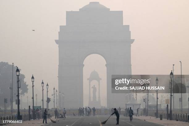 Workers clean the Kartavya Path in front of the India Gate amid heavy smoggy conditions in New Delhi on November 13, 2023. Delhi regularly ranks...