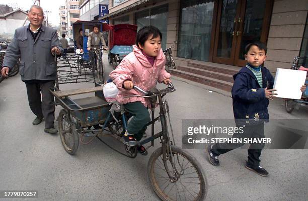 Grandfather walks with his grandson as he lets his granduaghter practice her peddling on the family tricycle down an alley in central Beijing 03...