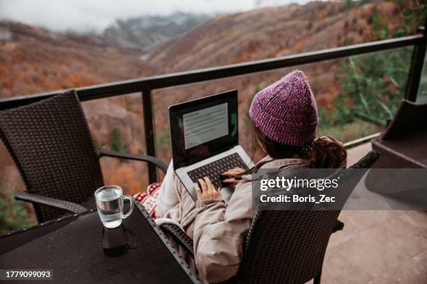 a young woman is working remotely from a mountain house with an incredible view, using her laptop - stock photo - log cabin porch stock pictures, royalty-free photos & images
