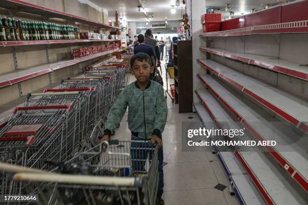 Palestinian boy stands near empty shelves at a supermarket in Rafah, in the southern Gaza Strip on November 13 amid the ongoing battles between...