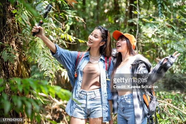 asian friend girls backpacker friend travel in forest wild together. attractive young two women traveler walk and exploring nature wood with happiness and fun during holiday vacation trip on summer. - girls trip film stockfoto's en -beelden