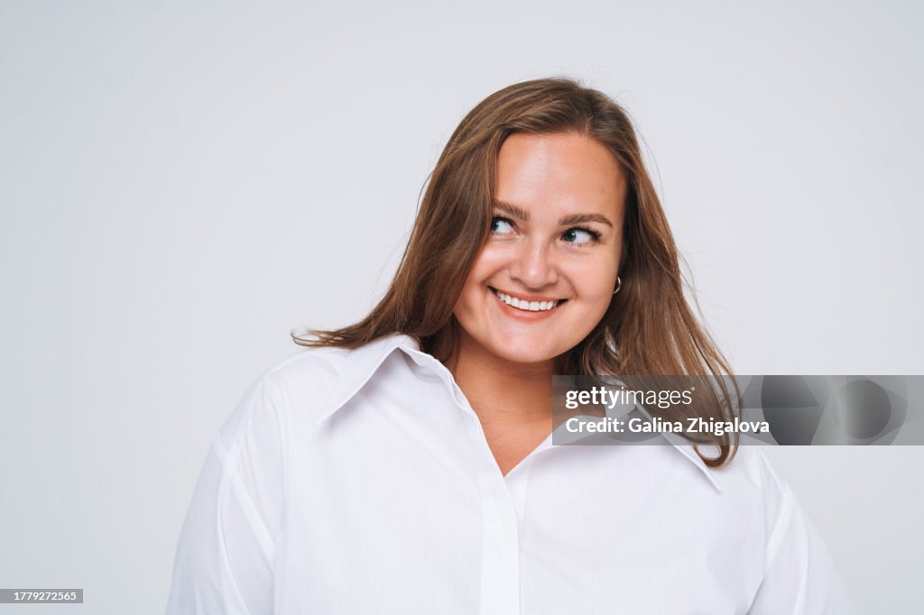 Portrait of smiling young brunette woman plus size in white shirt on white background